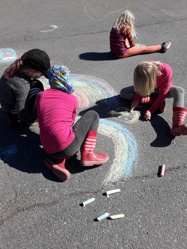 Lapsia piirtämässä asfalttiliiduilla koulun pihaan.