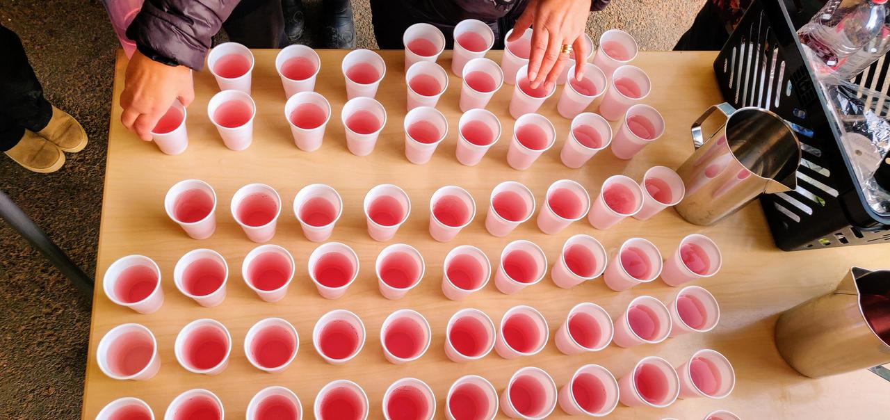 Kuva pihan avajaisten tarjoilupöydästä, jolla on paljon punaisella mehulla täytettyjä muovikuppeja.