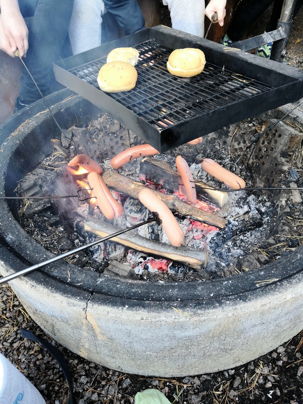 Kuvassa nuotiolla paistetaan makkaraa ja sämpylöitä.