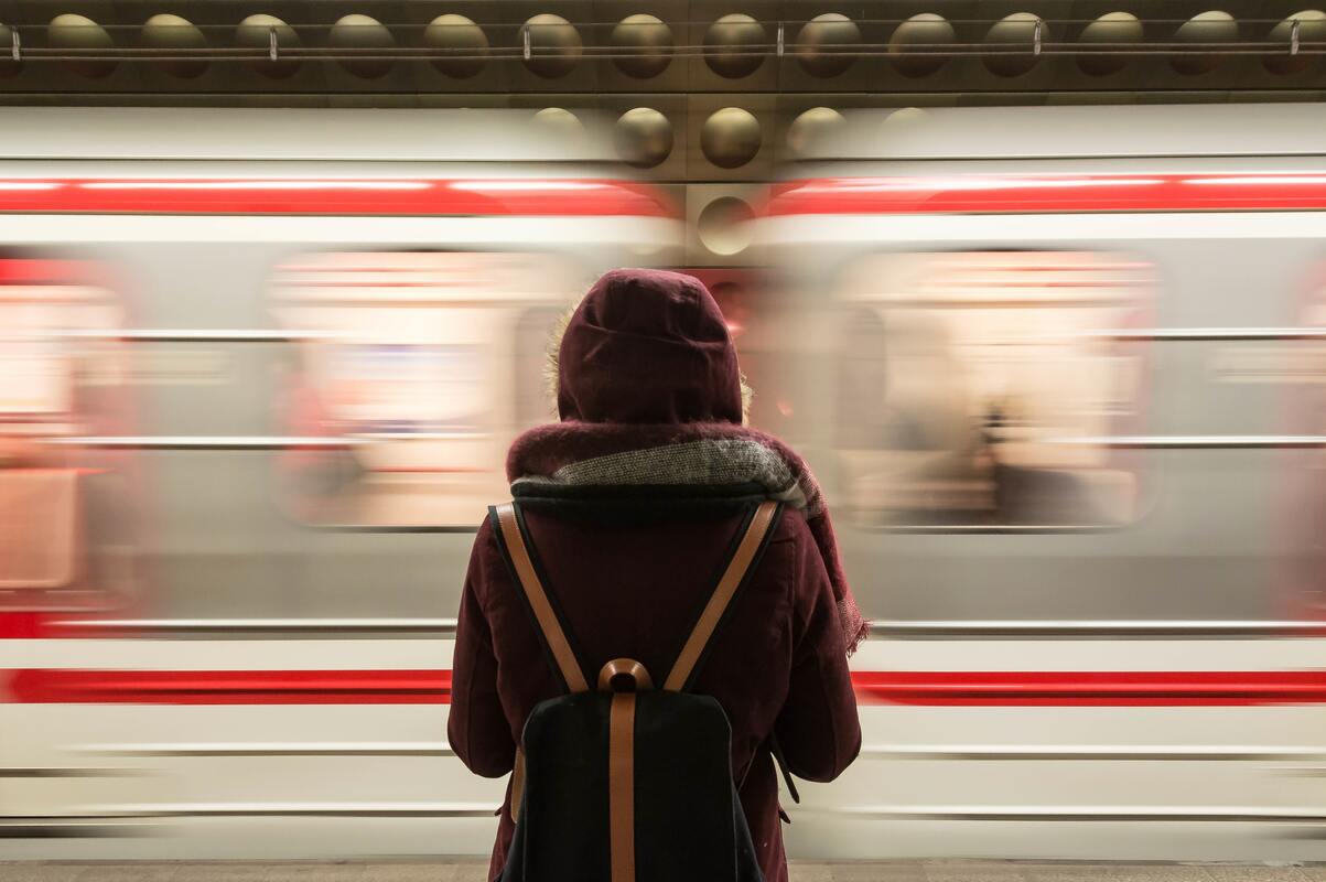 Huppupäinen ihminen reppu selässä on selin ja katsoo ohikiitävää junaa.