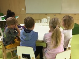 Lapset istuvat pöydän ääressä ja katsovat pöydällä olevia mittalaseja joissa on vettä.