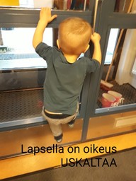 Lapsi roikkuu ovenkahvassa ja kiipeää ylös ovea pitkin: teksti kuvan päällä "lapsella on oikeus uskaltaa".
