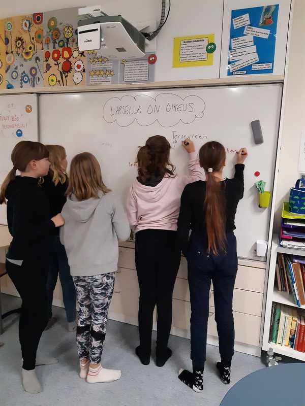 Oppilaat kirjoittavat taululle jokainen omalla tussillaan asioita Lapsella on oikeus -otsikon alle.