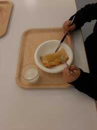 Oppilas syö kouluruokaa. Kuva otettu ylhäältä päin, lapsen kasvoja ei näy.