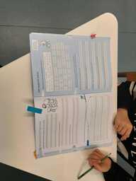 Oppilas kirjoittaa tehtäväkirjaan lyijykynällä. Kuva otettu ylhäältä päin, kasvot eivät näy.