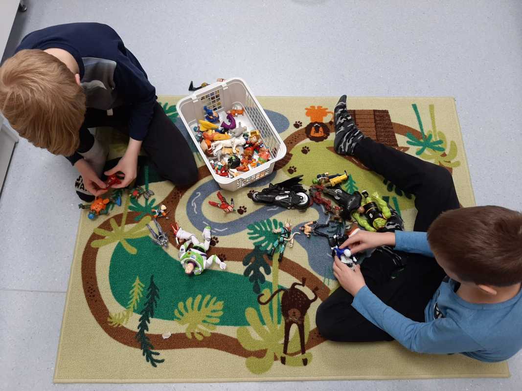 Lapset leikkivät leikkimaton päällä muovieläimillä. Kuva on otettu ylhäältä päin, lasten kasvot eivät näy.