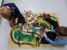 Lapset leikkivät leikkimaton päällä muovieläimillä. Kuva on otettu ylhäältä päin, lasten kasvot eivät näy.