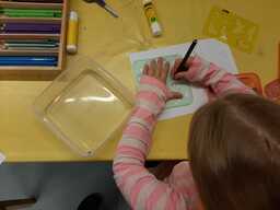Oppilas piirtää paperille lyijykynällä piirtosabloonaa käyttäen. Kuva otettu ylhäältä päin, kasvot eivät näy.