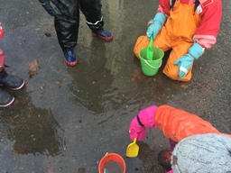 Neljä lasta on vesilätäkön ympärillä. Kaksi lapsista lapioi vettä.