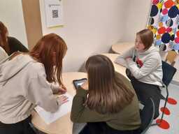 Oppilaat istuvat ryhmänä pöydän ääressä. Yksi kirjoittaa paperille ja muut tutkivat iPadilta tehtävää.