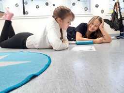 Kaksi oppilasta makaa lattialla ja täyttävät yhdessä tehtävämonistetta.