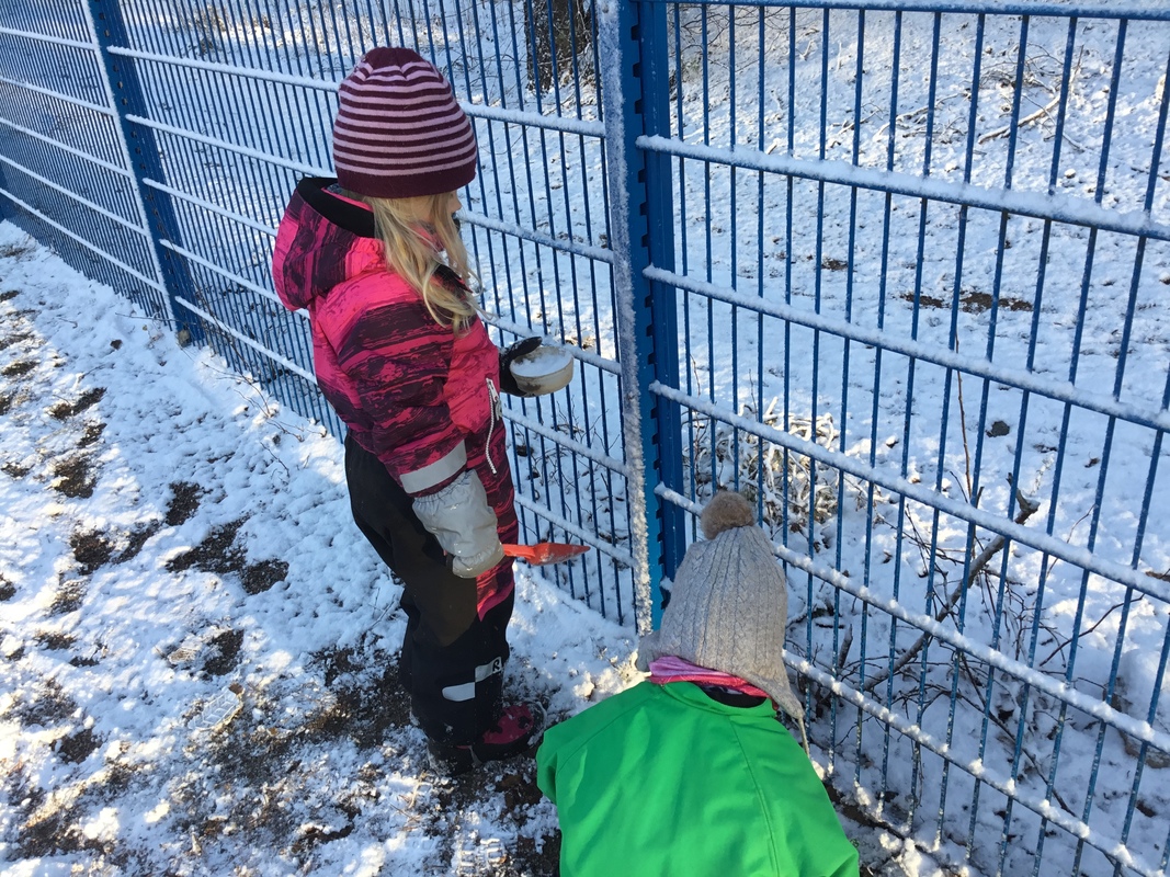 Kaksi lasta leikkii aidan edessä lumella.
