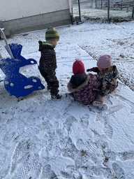 Kolme lasta leikkii maassa lumella.