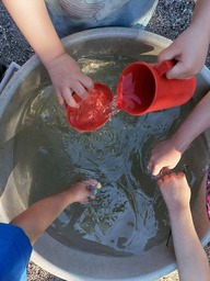 Käsiä vedessä leikkimässä ja kaatamassa kannusta vettä.