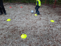 Lapsi pujottelee pallon kanssa merkkien välistä.