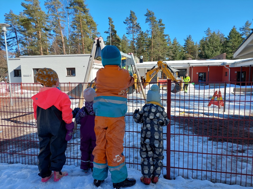 Lapset katselevat kaivinkonetta aidan takaa.