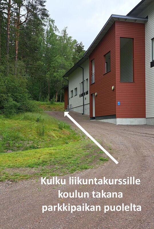 Sisäänkäynti liikuntakursseillemme kaukalon puoleiselle parkkipaikalle saavuttaessa: kävele koulurakennuksen viereistä hiekkatietä mäki ylös. Kulman takana on syvennys, jossa on portaat liikuntatiloihin.