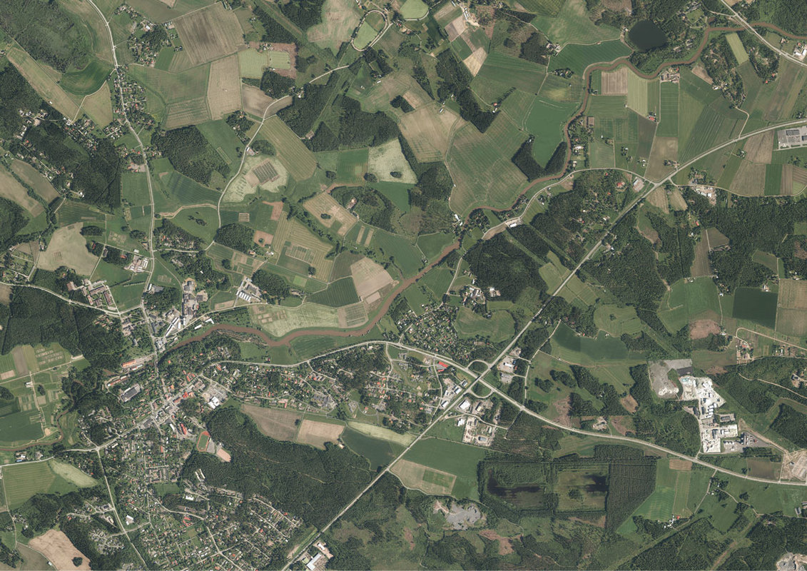 Ilmakuva. Oheisessa kuvassa tumman vihreä alue on metsää, vaaleat alueet ovat peltoja. Kuvan läpi virtaa joki. Lisäksi kuvassa näkyy taajama-alueen asutusta ja tieverkostoa.