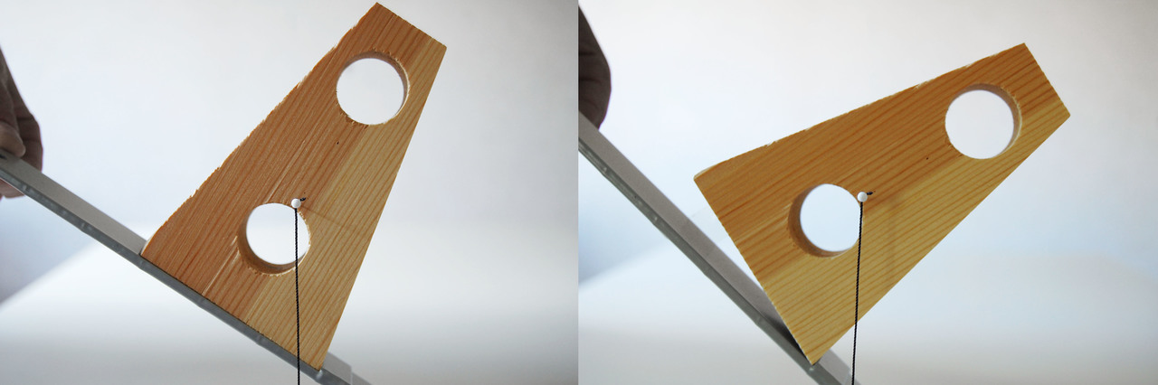 A wooden object falls down from a slanted metal surface when its center of gravity (the black string) moves outside its supporting surface.