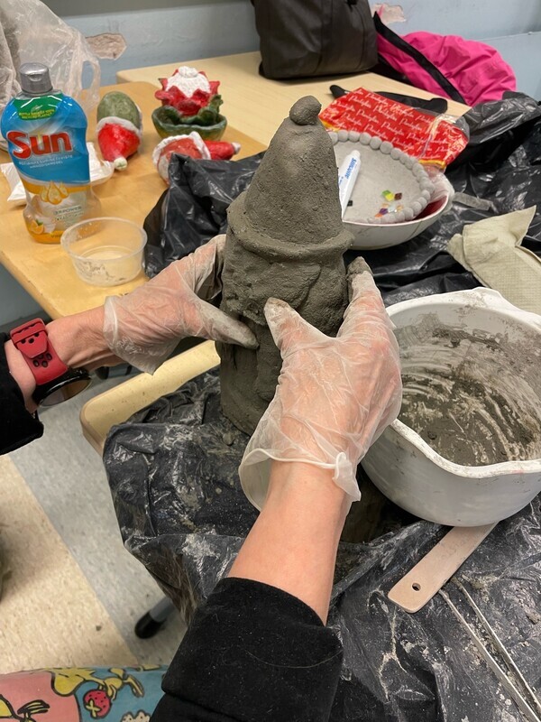 Kuvassa kädet muotoilevat tonttupatsasta savesta.