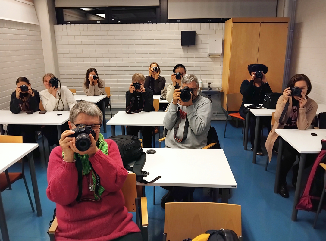 Kuvassa luokassa opiskelijoita, joista kaikki ottavat kuvaa edessä olevasta opettajasta.